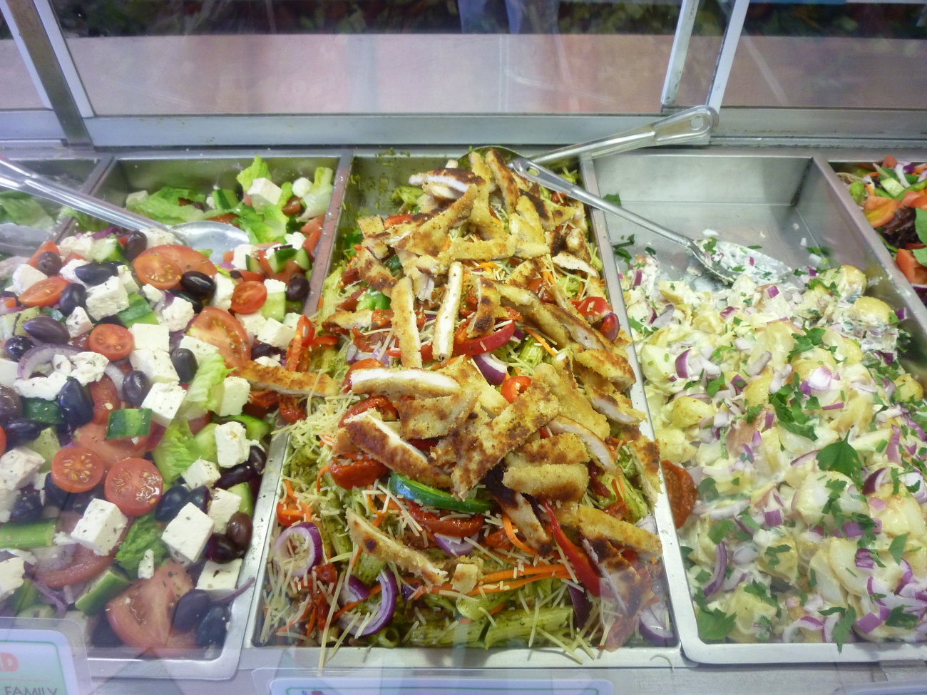Three trays in the salad bar: Greek salad with feta and olives, crumbed chicken on slaw, and potato salad