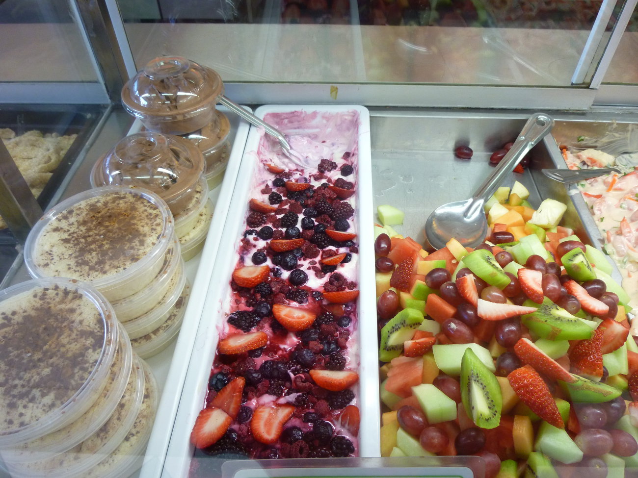 Tubs of rice custard beside trays of triple berry yogurt and fresh fruit salad